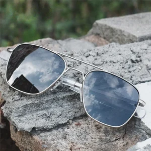 Óculos Yellowstone - armação prateada robusta com lentes escuras refletindo o céu sobre superfície de concreto - Solluss Óculos Yellowstone - detalhe frontal da ponte dupla em metal prateado e lentes escuras - Solluss Óculos Yellowstone - vista lateral destacando o acabamento polido da armação masculina - Solluss